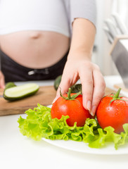 Closeup of pregnant woman taking fresh tomato from plate