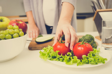 Obraz na płótnie Canvas toned photo of woman picking fresh tomato from table on kitchen