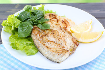 Dish of fish fillet with greens and lemon on table close up