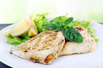 Dish of fish fillet with greens and lemon on bright background