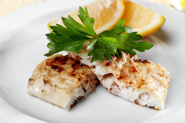 Dish of fish fillet with greens and lemon on plate close up