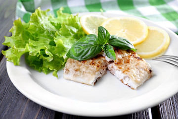 Dish of fish fillet with greens and lemon on plate close up