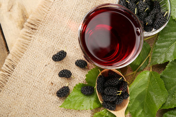 Glass of refreshing mulberry juice with berries on table close up
