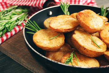 Delicious baked potato with rosemary in frying pan on table close up