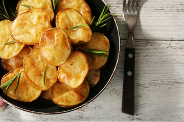 Delicious baked potato with rosemary in frying pan on table close up