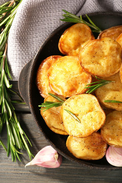 Delicious baked potato with rosemary in frying pan on table close up