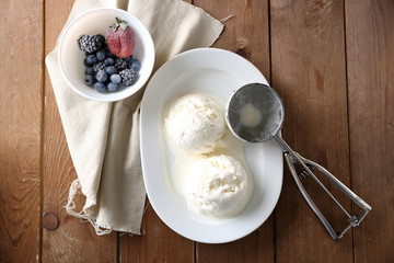 Delicious vanilla ice cream on plate, on wooden background