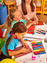 Kids holding colored paper on table in kindergarten .