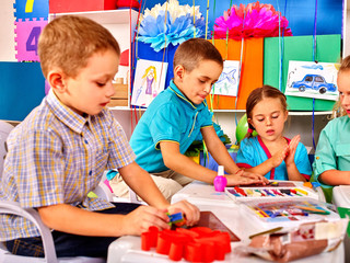 Kids holding colored paper on table in kindergarten .