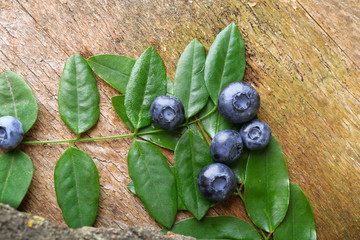 Fresh blueberries with green leaves on wooden table, closeup