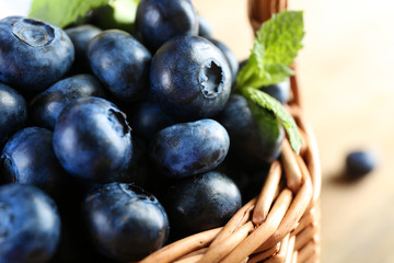 Tasty ripe blueberries with green leaves in basket close up