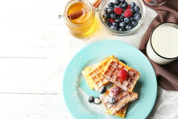 Sweet homemade waffles with forest berries on plate, on light background