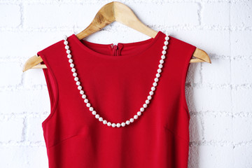 Blouse and necklace on hanger on wall background