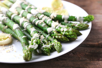 Appetizing asparagus in sour cream sauce with onion and cheese on white plate against wooden background