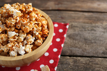 Sweet caramel popcorn in a bowl on red cotton napkin against wooden background