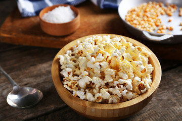 Salted popcorn in a bowl decorated with kitchen equipment on wooden table