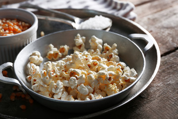 Salted popcorn in a metal bowl with cup of corns on wooden table