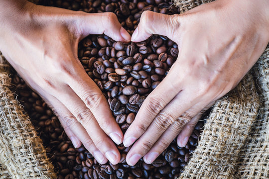 closeup coffee beans in hands of heart shaped with sunlight in gunny bag. i love coffee