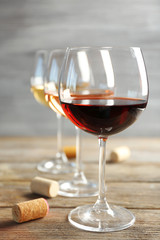 Wine glasses in a row and corks on wooden table against grey background