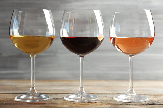 Wine glasses in a row on wooden table against grey background