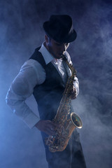 Fototapeta na wymiar Elegant saxophonist plays jazz on dark background in blue smoke
