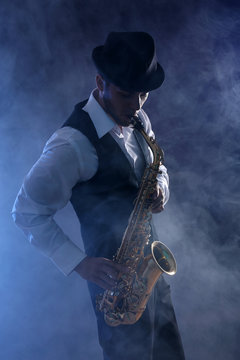 Elegant saxophonist plays jazz on dark background in blue smoke
