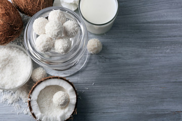 Candies in coconut flakes and fresh coconut on color wooden background