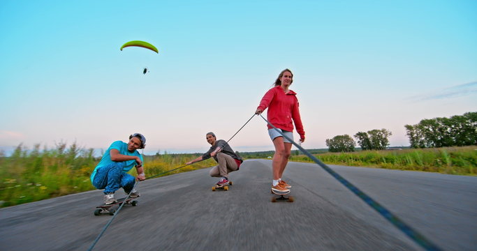 Friends are riding longboards and holding rope together