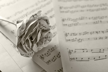 Naklejka premium Single white paper-made rose on musical notes pages background