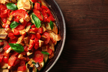 Tasty vegetarian ratatouille made of eggplants, squash, tomatoes and onions in black cast iron pan, on wooden table background