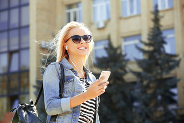 Obraz premium Young woman listening to music and walking along the street