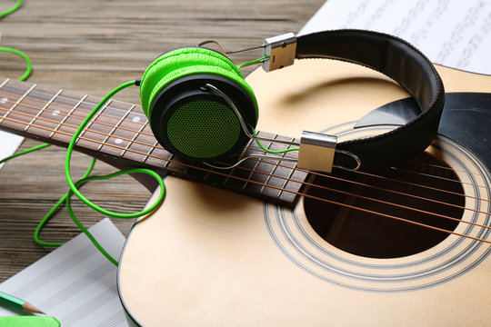 Classical guitar and headphones with notes on wooden background