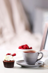 Beautiful chocolate cupcake with raspberry and cup of tea, on table