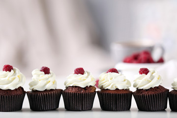 Beautiful chocolate cupcakes with cream and raspberry on table