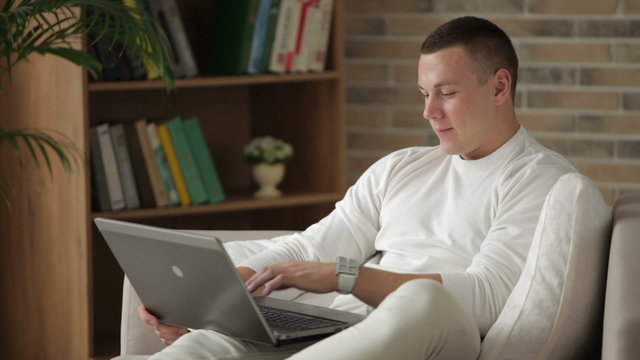 Attractive young man sitting on sofa with laptop closing it and smiling
