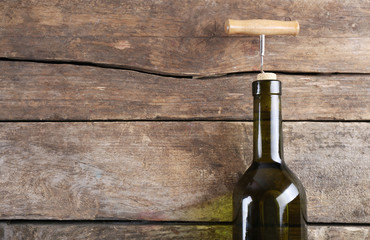 Bottle of wine with corkscrew on wooden background