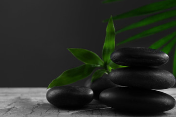 Obraz na płótnie Canvas Black spa stones and green flowers, on dark grey background