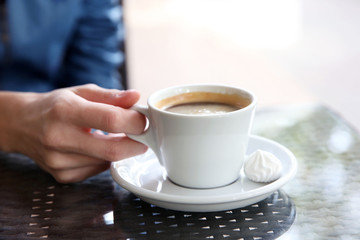 Cup of coffee with hands and zephyr on table in cafe background