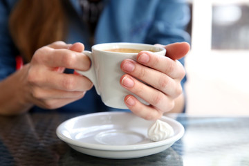 Cup of coffee with hands and zephyr on table in cafe background