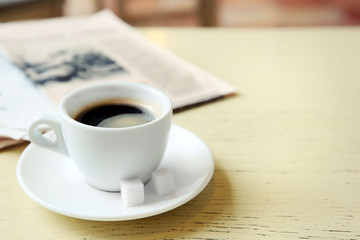 Cup of tasty coffee with newspaper and sugar on table