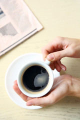 Cup of coffee with hands and newspaper on table