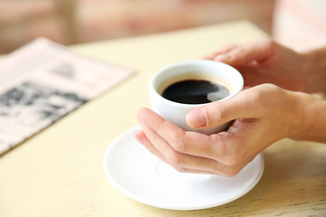 Cup of coffee with hands and newspaper on table in cafe background
