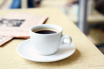 Cup of tasty coffee and newspaper on cafe background
