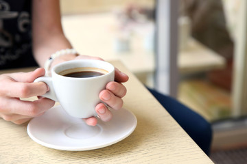 Cup of coffee with hands on table in cafe background