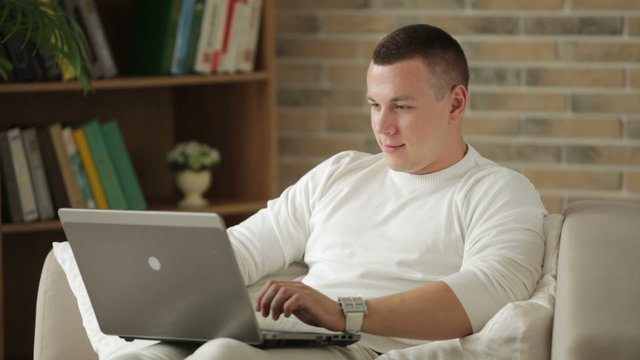 Handsome guy sitting on couch with laptop holding credit card and smiling