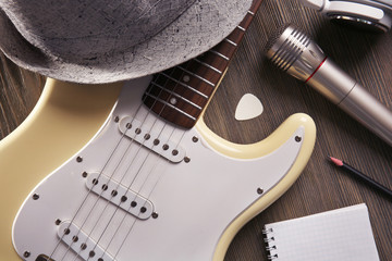 Electric guitar with headphones, hat and microphone on wooden background, close up