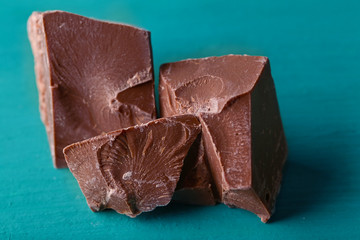 Milk chocolate pieces on color wooden background
