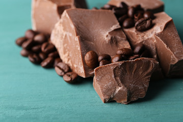 Milk chocolate pieces and coffee grains on color wooden background