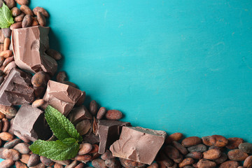 Dark and milk chocolate pieces and cocoa beans on color wooden background