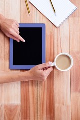 Overhead of feminine hands using tablet and holding coffee